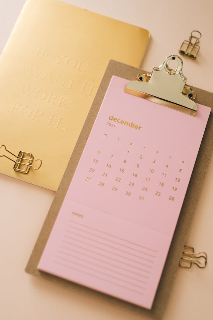 Aesthetic pink December calendar on clipboard with gold accents and binder clips.